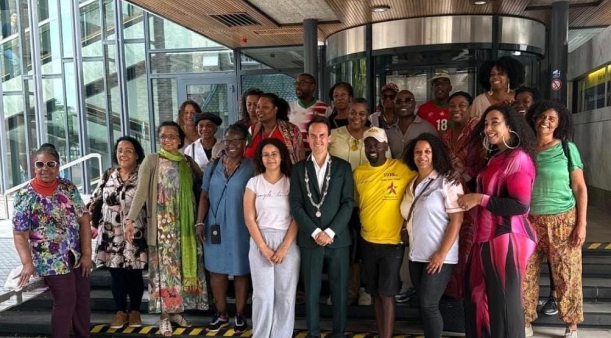 Stephen Brug in gele Loop Voor Hoop Tshirt, geflankeerd door Arnhems loco burgemeester Paul Smeulders (links) en raadslid Nathalie Nede (ChristenUnie), alsook mensen uit de Surinaamse gemeenschap van de stad