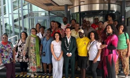 Stephen Brug in gele Loop Voor Hoop Tshirt, geflankeerd door Arnhems loco burgemeester Paul Smeulders (links) en raadslid Nathalie Nede (ChristenUnie), alsook mensen uit de Surinaamse gemeenschap van de stad